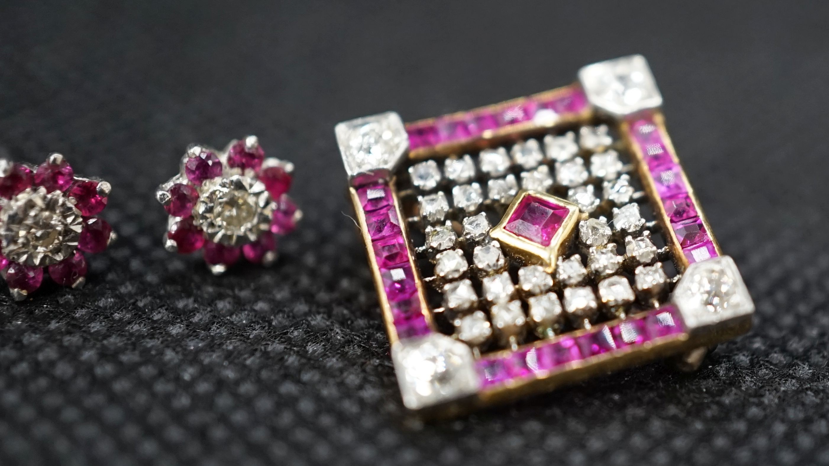 An early 20th century pierced yellow metal, ruby and diamond cluster set square brooch, 17mm and a pair of white metal, ruby and diamond cluster flower head ear studs, gross weight 5.8 grams.